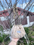 Load image into Gallery viewer, Full-size Beige Bloom quilted Mochi bag held outdoors with matching floral shoulder strap

