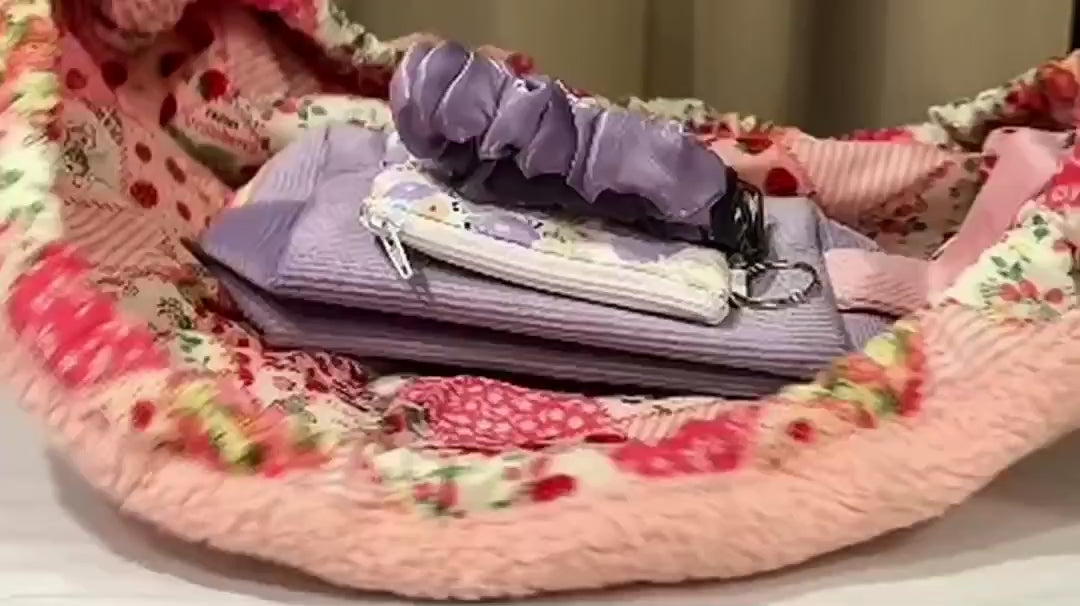 A pink Mochi bag opens flat to show makeup and everyday essentials, then gathers closed with its drawstrings.